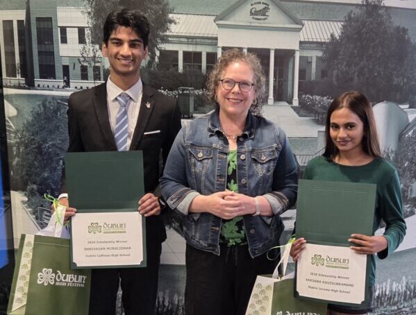 2026_festival_scholarship_winners Three smiling students stand with certificates and gift bags in front of a school backdrop, posing for an award photo.
